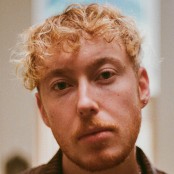 A close up image of a person with blonde curly hair and one ear piercing